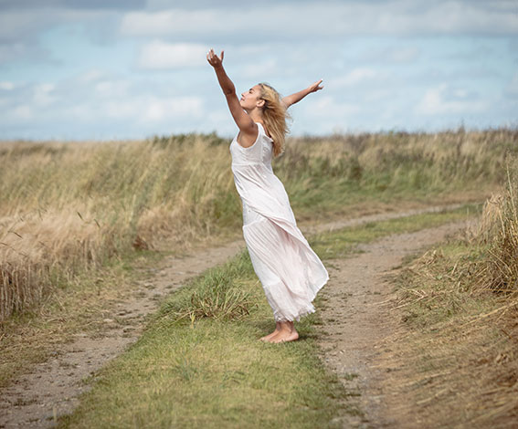 Femme en robe qui écarte les bras dans un champ